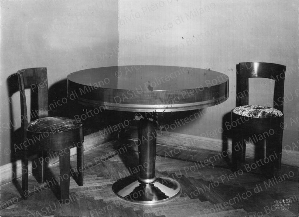 Veduta di tavolo da pranzo con 2 sedie. Timbro a secco "Paoletti fotografo Milano". Positivo, bianco e nero, 160x222 mm, album giallo n.8, pag.36.