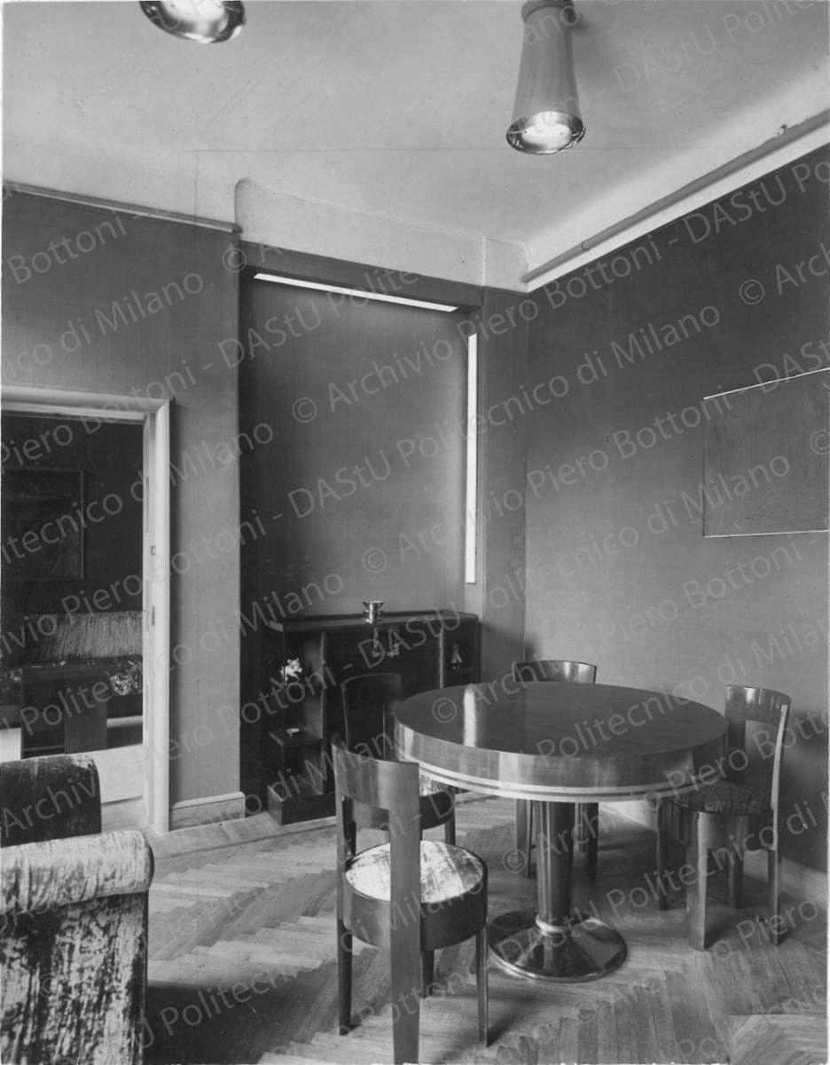 Veduta del soggiorno e della sala da pranzo con tavolo, sedie, 'credenza da salotto' e poltrone. Positivo, bianco e nero, 282x219 mm, album giallo n. 8, pag. 37.