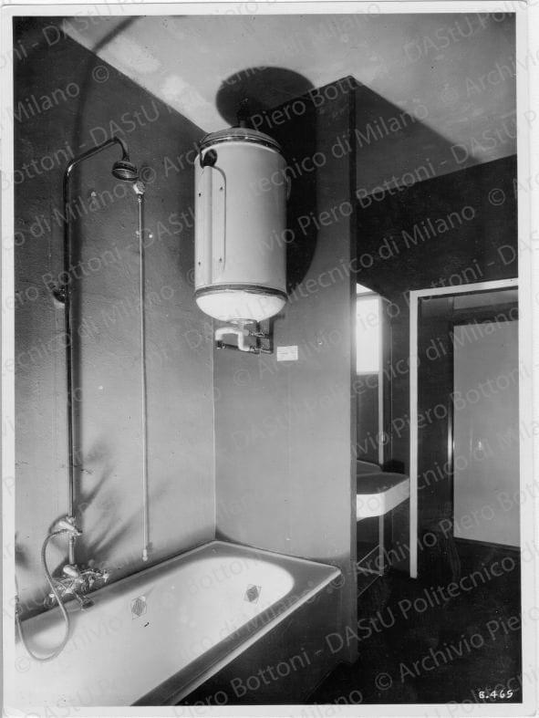 Veduta del "Bagno", positivo, bianco e nero, mm 222x163.  Timbri ad inchiostro sul verso: "Piero Bottoni", "Da restituire" e "La propriet? di questo modello ? protetta a norma dell'art. 1 e seg. Del R.D. del 7nov. 1925 n. 1950 sul diritto d'autore". Annotazione dattiloscritta su carta velina e incollata sul verso della fotografia: "Bagno. Nella "Casa elettrica" a Monza - Progettato dell'Arch. Piero Bottoni - Corso Roma 101 - Milano. Rivestimento delle pareti in materiale gommato lavabile (arancione e azzurro): pavimento in mosaico unicolore di ceramica (viola-grigio). Zoccolino in linoleum nero. Vasca incassata, scaldabagno elettrico. In fondo mobile da toletta per accappatoi, asciugamani e profumi, psiche con luce laterali. "Annotazione fotografica sul recto della fotografia: "B. 465".