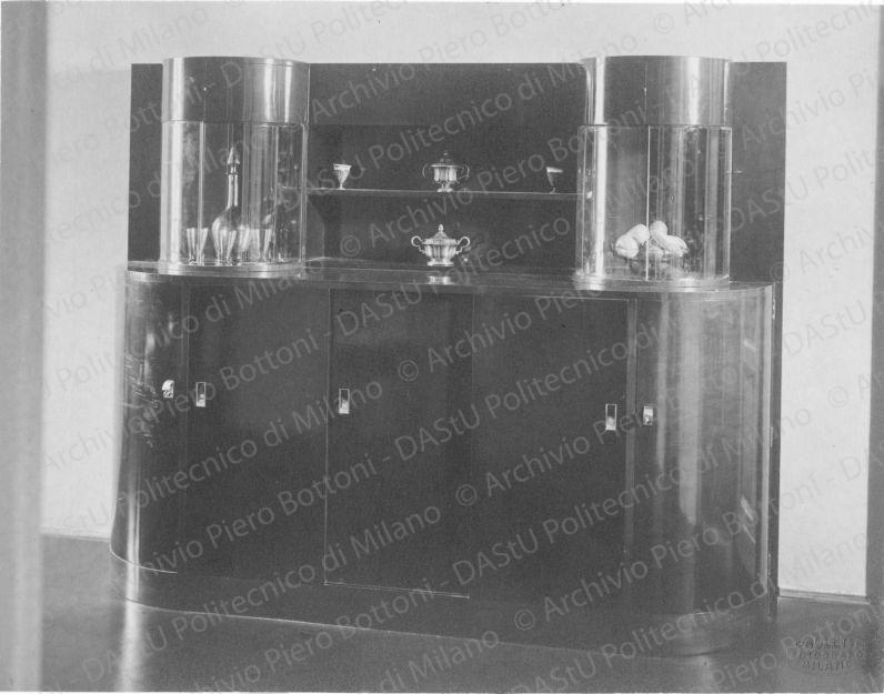 Veduta della credenza. Didascalia dattiloscritta: "Credenza di salotto da pranzo in casa Minerbi a Milano. Vetrina a cristalli scorrevoli; sportelli scorrevoli; ripiani, cassetti, cassettini per servizi". Timbro a secco "Paoletti fotografo Milano". Positivo, bianco e nero, 157x203 mm, album giallo n.8, pag.63.
