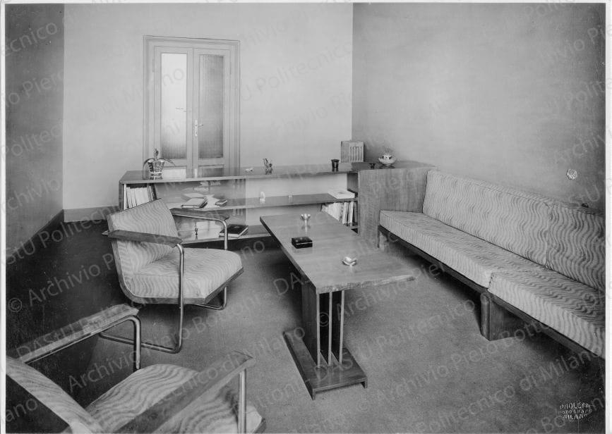 Veduta di "Locale di soggiorno e di lavoro", positivo, bianco e nero, mm 210x292. Timbri ad inchiostro sul verso: "Piero Bottoni" e "Da restituire". Annotazione manoscritta sul verso: "Casa Franceschini. Locale di soggiorno e di lavoro. V. descrizione altra foto. Scaffale libreria a doppia faccia con parete divisoria in vetro placcato paglierino. A sinistra armadietto da lavoro. Nello sfondo, divano, tavolino, poltrona in tubo di acciaio, mobiletto per lavoro. Pavimento in linoleum rosso arancione. Legno di noce chiaro. Tappezzeria terra-siena e bianco sporco".