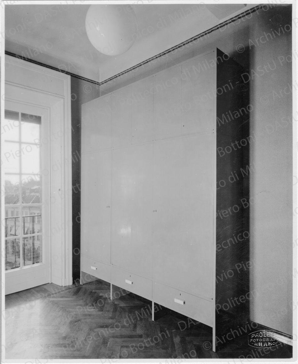 Veduta di "Mobile grande di guardaroba", positivo, bianco e nero, mm 198x161.  Timbri ad inchiostro sul verso: "Piero Bottoni" e "Da restituire". Annotazione dattiloscritta sul verso: "Mobile grande di guardaroba in casa Ing. B. A. Milano. Sportelli, ante e cassetti con maniglie in galattite. Tinteggiatura grigio-azzurra alla nitrocellulosa."