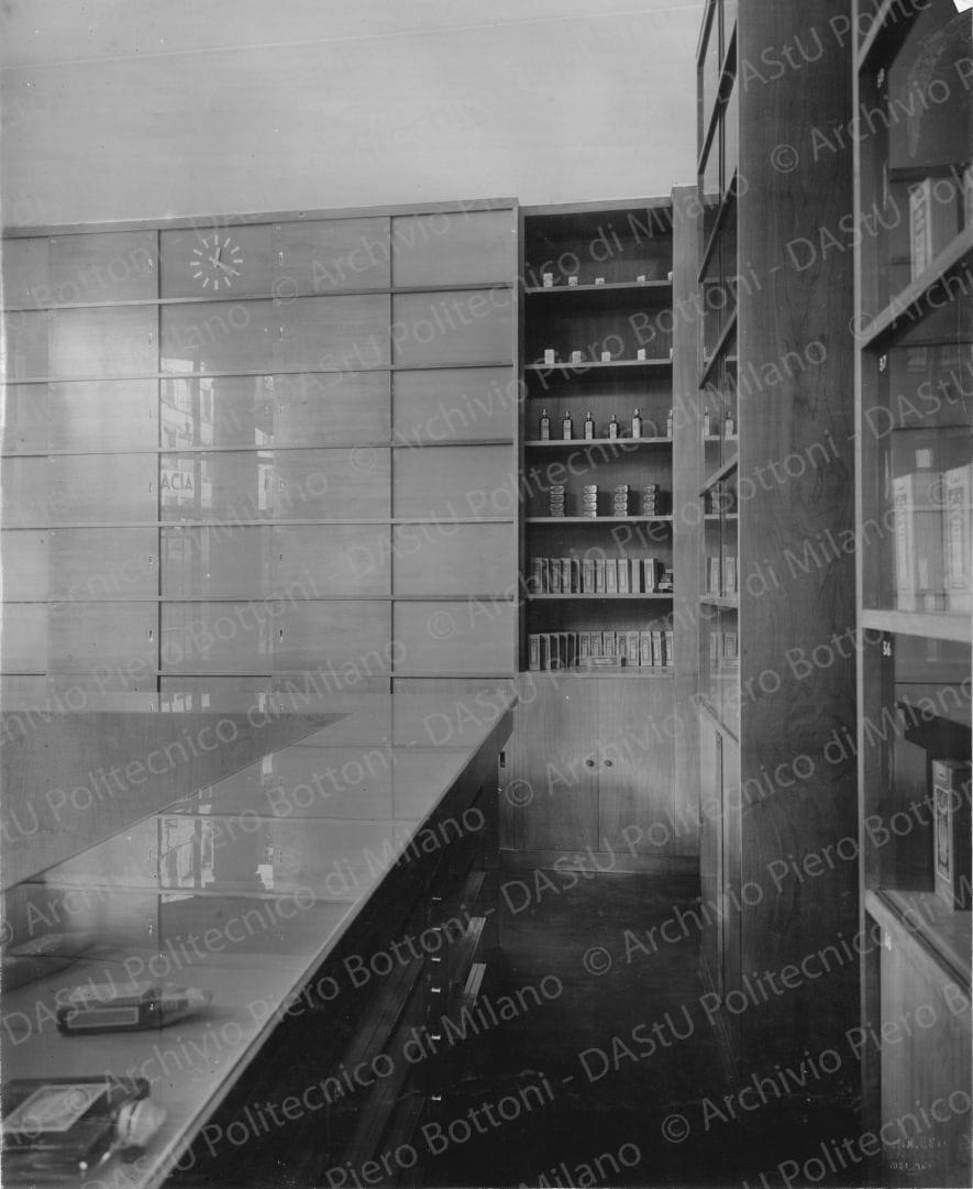 Veduta del banco di vendita e degli armadi dei medicinali. Timbro a secco "Paoletti fotografo Milano". Positivo, bianco e nero, 276x225 mm, album giallo n.6, pag.5.