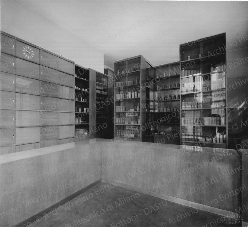 Veduta del banco di vendita e degli armadi dei medicinali. Timbro a secco "Paoletti fotografo Milano". Positivo, bianco e nero, 195x215 mm, album giallo n.6, pag.6.