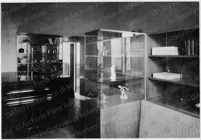 Veduta della vetrina, positivo, bianco e nero, mm 158x230. Timbro ad inchiostro sul verso: "Piero Bottoni". Annotazione dattiloscritta su carta velina e incollata sul verso della fotografia: "Dettaglio della vetrina; della libreria a vetri scorrevoli e del divano visti dal salottino; in fondo il pianoforte e dietro l'armadio per i servizi da tavola del passapiatti e la doppia porta della cucina".