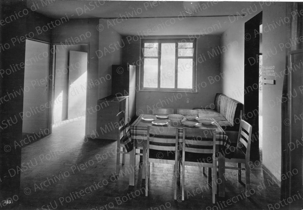 Veduta interna del soggiorno dell'alloggio tipo n. 1. Didascalia: 'Alloggio n. 1 con accesso dal ballatoio. Il locale di soggiorno su corpo doppio con vista nello sfondo letti. Mobili in ontano naturale con piani in linoleum (esecuzione Meroni e Fossati). Positivo, bianco e nero, 156x225 mm, album giallo n. 7, pag. 40.