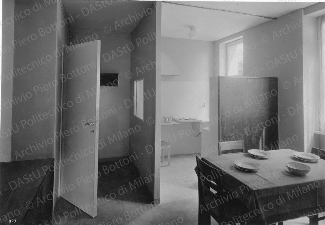 Veduta interna del soggiorno dell'alloggio n. 4. Didascalia: 'Ingresso, soggiorno, cucina comunicanti divisi da pareti, mobili, tende; il mobilio è lucidato noce o laccato, con piani in linoleum'. Positivo, bianco e nero, 157x226 mm, album giallo n. 7, pag. 48.