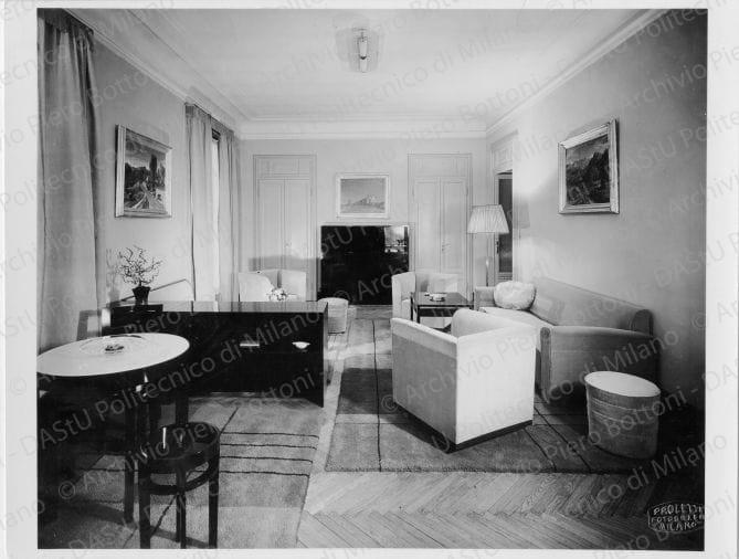 Veduta del "Salotto", positivo, bianco e nero, mm 172x226. Annotazione dattiloscritta su carta velina incollata sul verso: "Appartamento Dott. Cicogna Milano. Mobili e tappeti per salotto in ambiente (porte e soffitto esistenti) a sin. tavolo da gioco, al centro divani e poltrone (2 gruppi di ricevimento) in fondo mobile bar e servizi. Mobili in legno di pero tinteggiato verde scuro e nero e poltrone divani in velluto". 