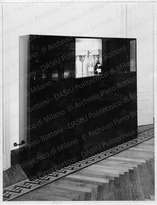 Veduta del "Mobile per servizi e bar", positivo, bianco e nero, mm 220x171. Timbro ad inchiostro sul verso: "Piero Bottoni" e annotazione dattiloscritta su carta velina incollata sul verso: "Appartamento Dott. Cicogna Milano. Mobile per servizi e bar in legno di pero lucidato verde scuro e nero e cristalli fumé scorrevoli".