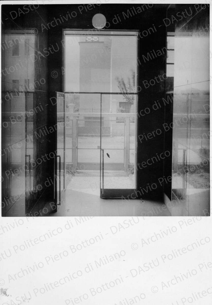 Idem, in formato differente, positivo, bianco e nero, mm 180x125. Annotazione dattiloscritta su velina incollata sul verso della fotografia: "...Atrio dell'ingresso dalla strada. Pareti e pavimento in botticino. Pareti in rosso di Verona. A destra la grande vetrata della portineria".