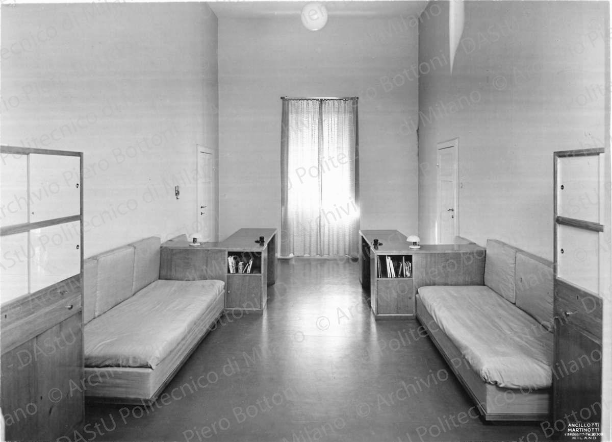 Veduta della camera da letto dei ragazzi. Didascalia dattiloscritta: "CASA BEDARIDA - LIVORNO - Architetti PIERO BOTTONI & MARIO PUCCI - Milano. La camera da letto dei ragazzi nel suo aspetto diurno. I mobili scrivania dividono la lunghezza della camera in due zone: la più luminosa per lo studio la più raccolta per il riposo. Per la notte due divani si trasformano in letti con accanto i rispettivi tavolini di servizio. Gli armadi sono divisi in reparti, per i libri, per i giuochi e per i vestiti. I mobili sono in rovere chiaro; le antine degli armadi sono laccate in verde Nilo i piani in opalina verde chiaro. Pavimento in linoleum bianco". Annotazione tipografica sul recto della fotografia: "Ancilotti Martinotti v. Broggi 17 tel 20309 Milano". Positivo, bianco e nero, 161x221 mm, album giallo n.8, pag.91.